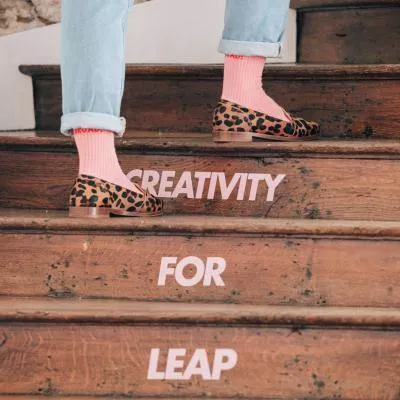 Un escalier en bois gravi par une personne en jean et mocassins léopard, dont les marches composent la phrase « a giant leap for creativity »